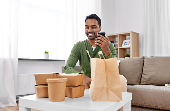 Man on couch with phone, holding food bag.